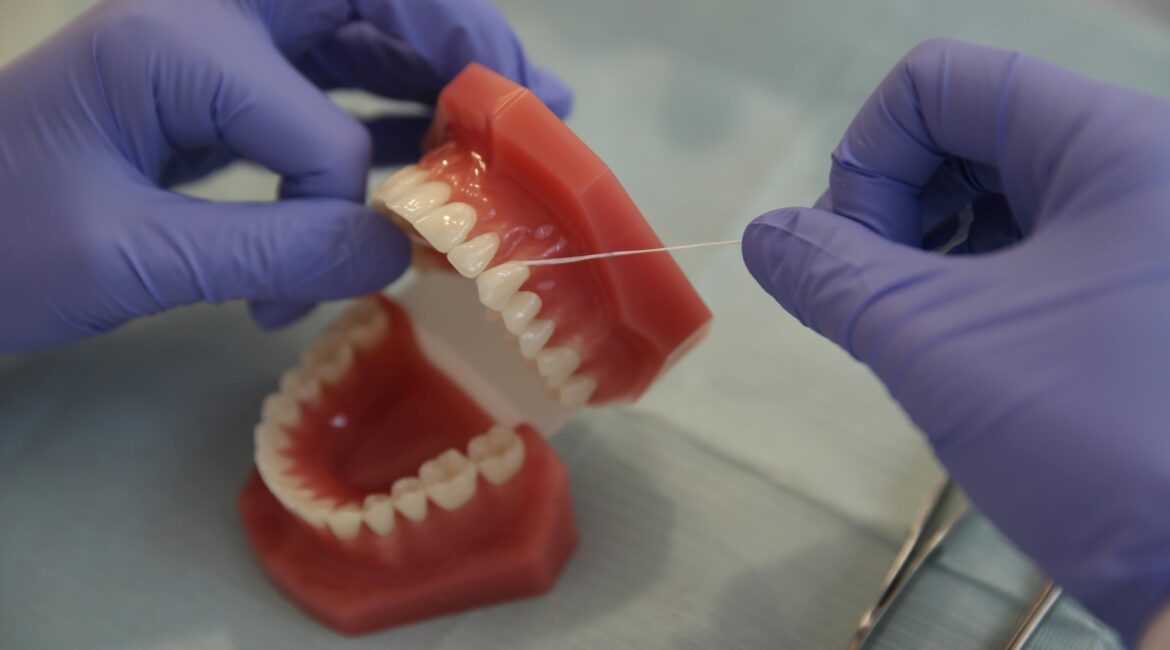 Close-up of a dental professional using floss on a denture model, emphasizing hygiene.