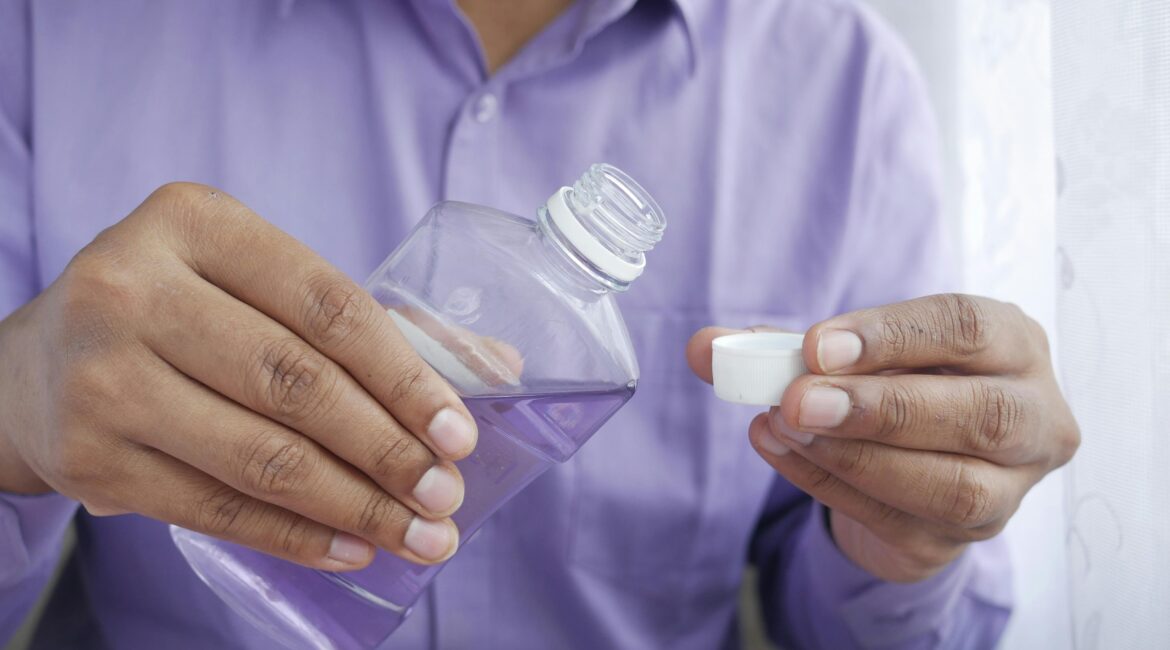 Close-up of hands holding a purple plastic bottle while pouring mouthwash into a cap.